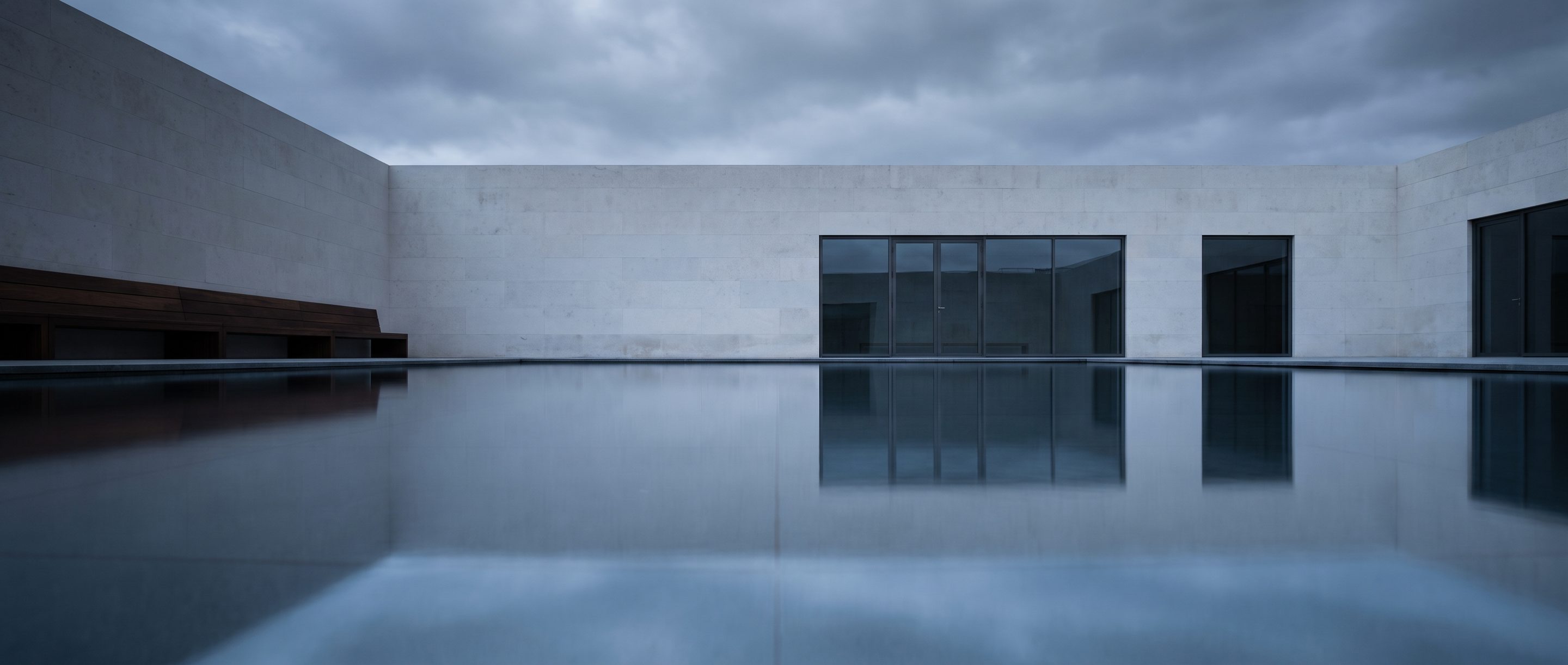 A still reflecting pool against a plain stone wall, overcast light.