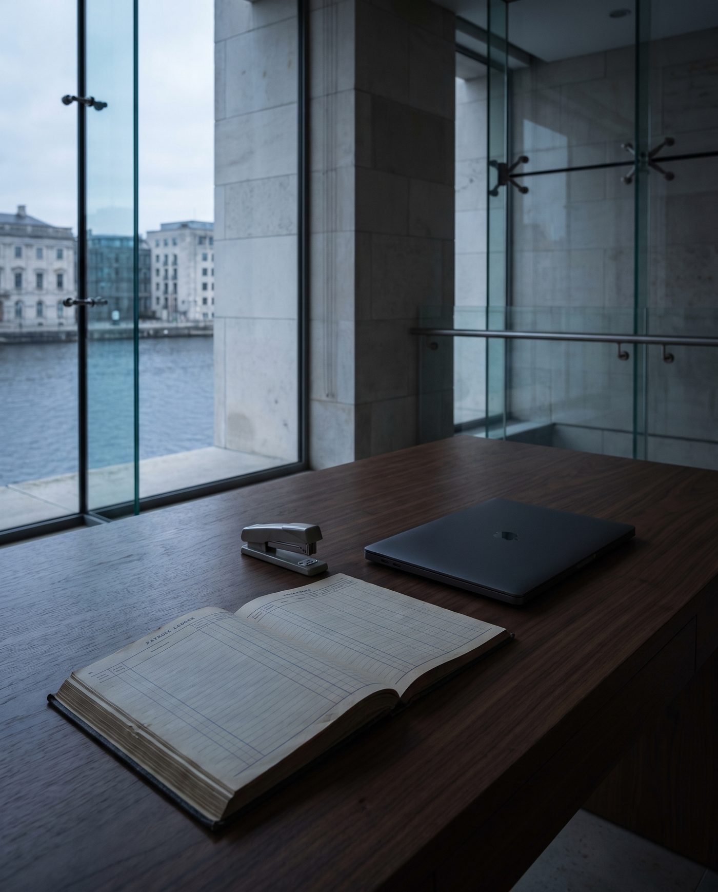 A payroll ledger and a stapler on a walnut desk beside a closed laptop.