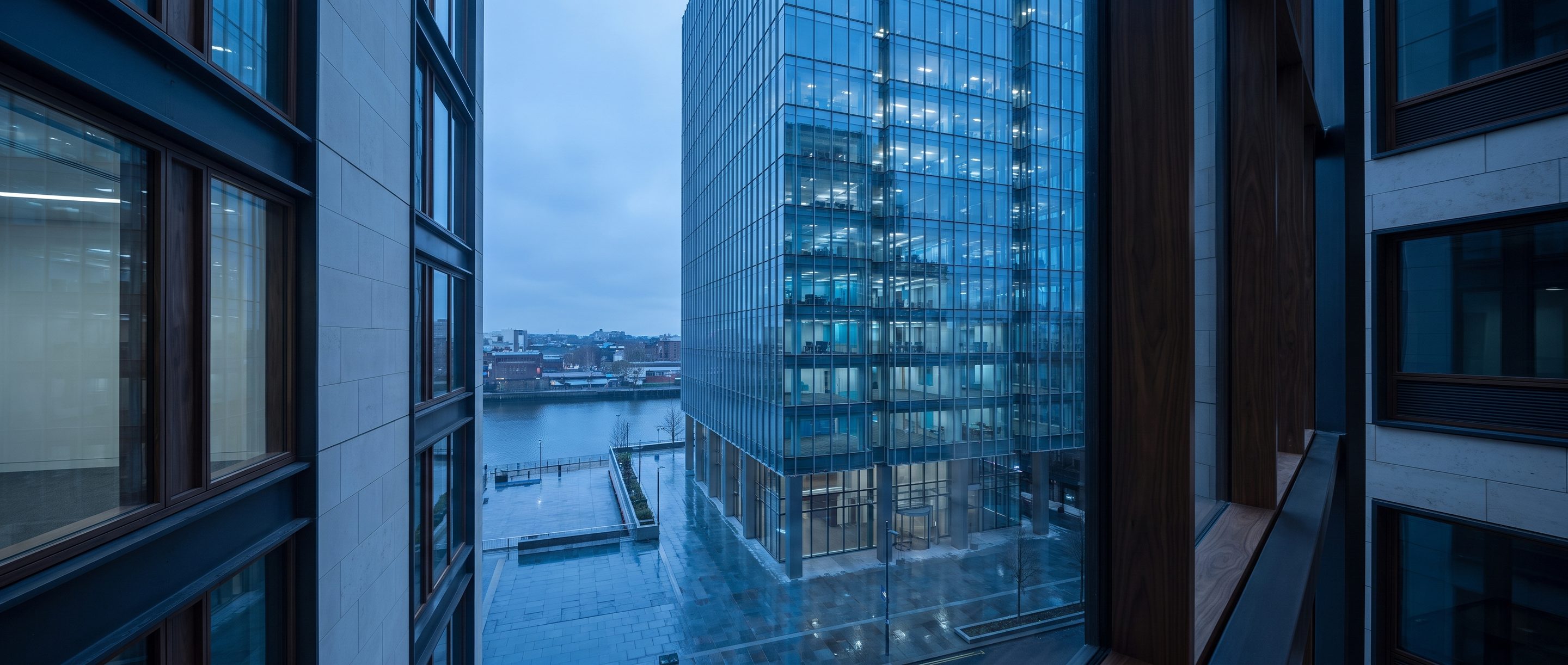A glass office tower at blue hour seen from a high window.