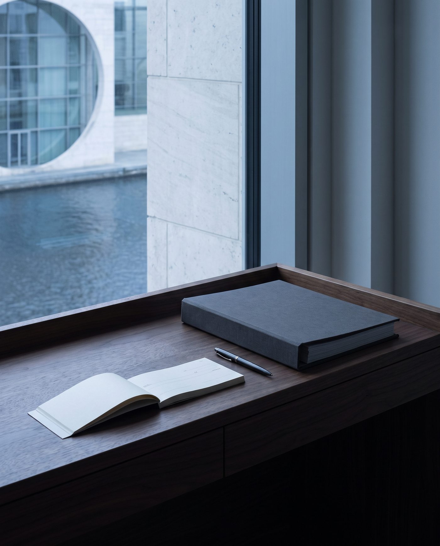 An open cheque book and a pen on a walnut desk beside a closed folder.