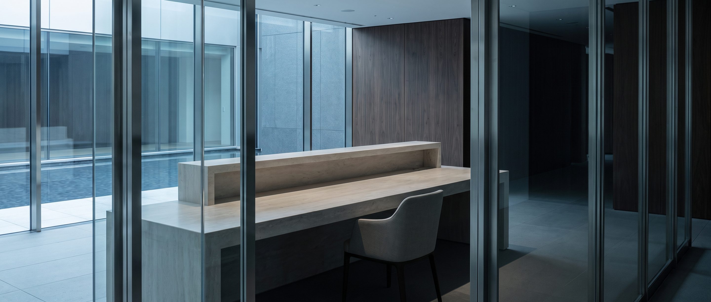A quiet office reception desk, pale stone counter, one empty chair.