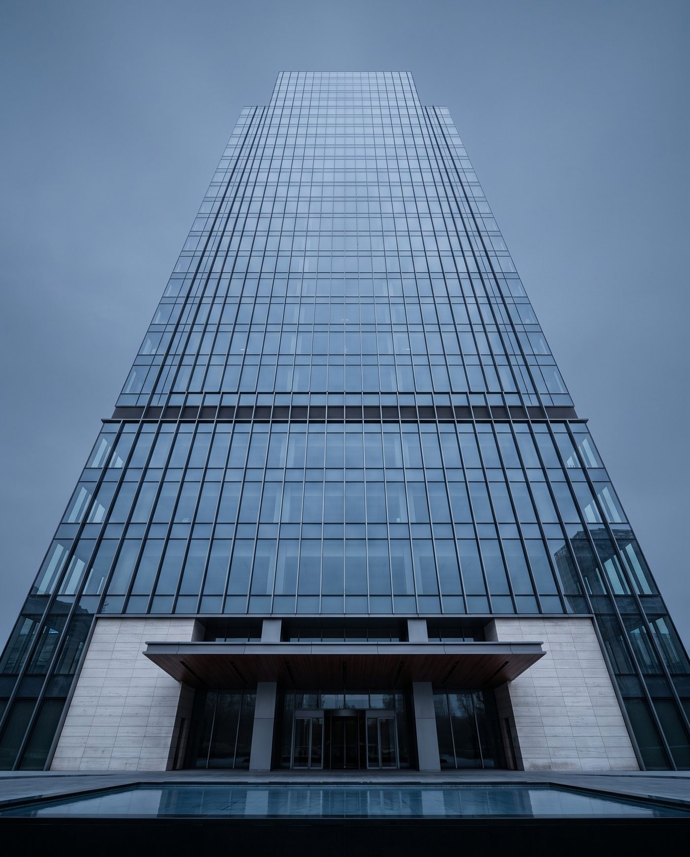 A glass office tower seen from below at a steep angle, overcast sky.