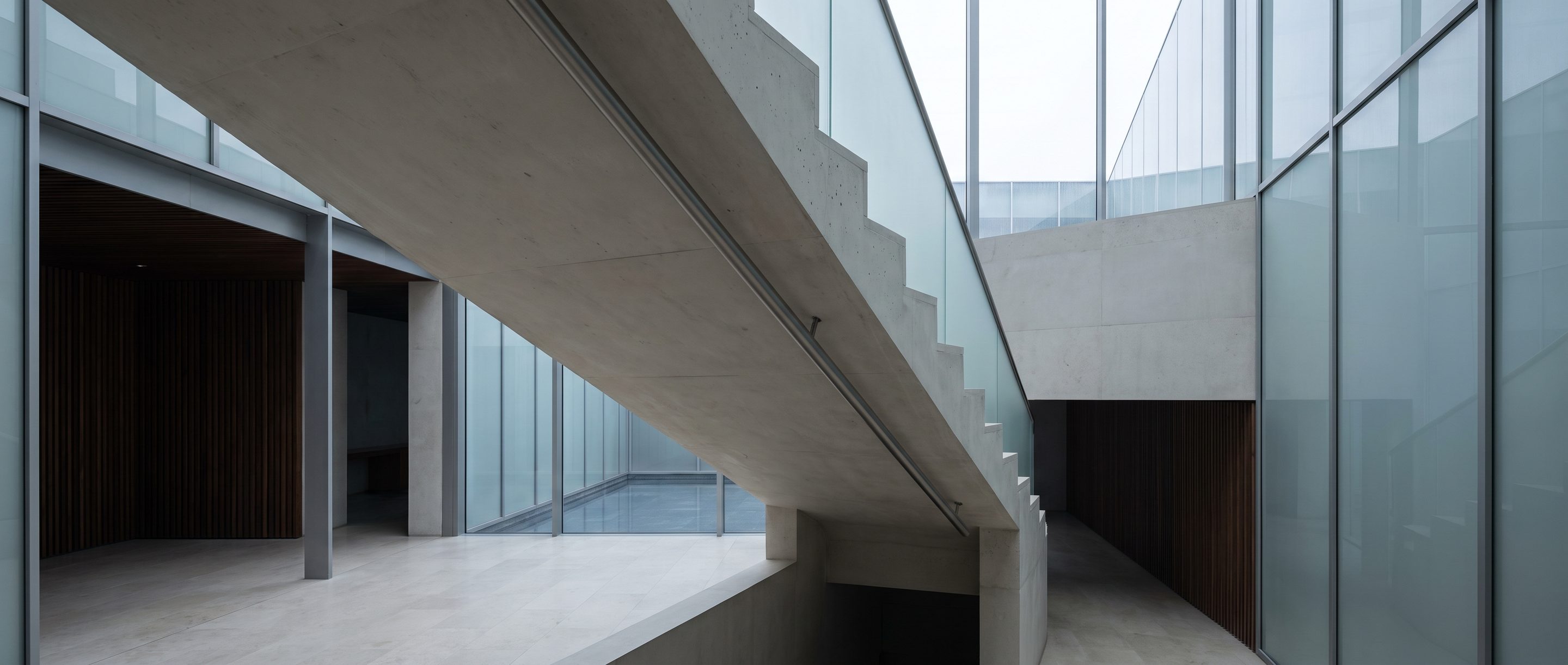 The underside of a pale concrete stair in an empty atrium.
