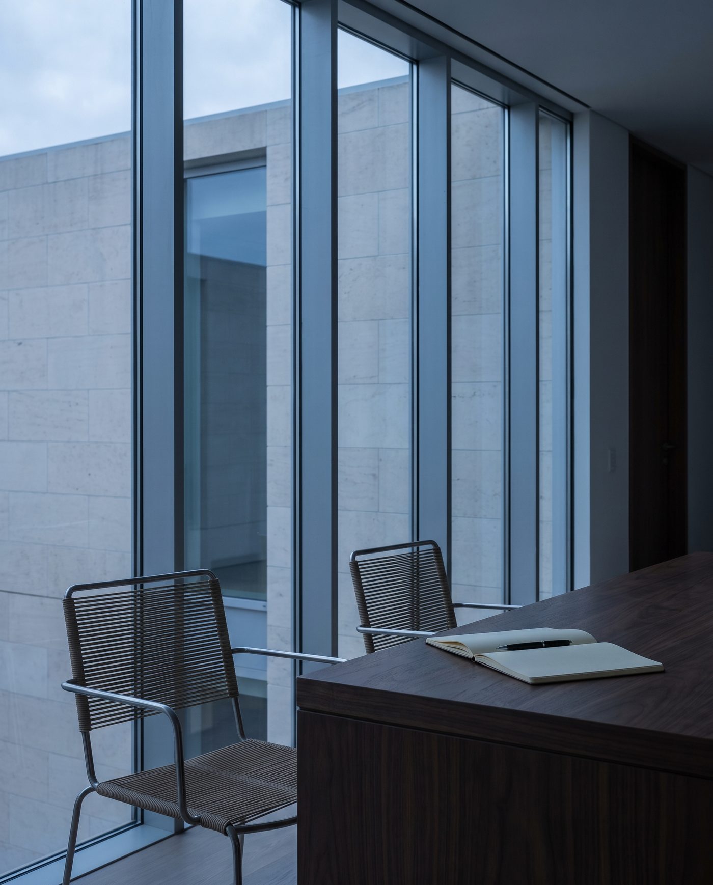 A note pad and a pen on a walnut table beside two empty chairs.