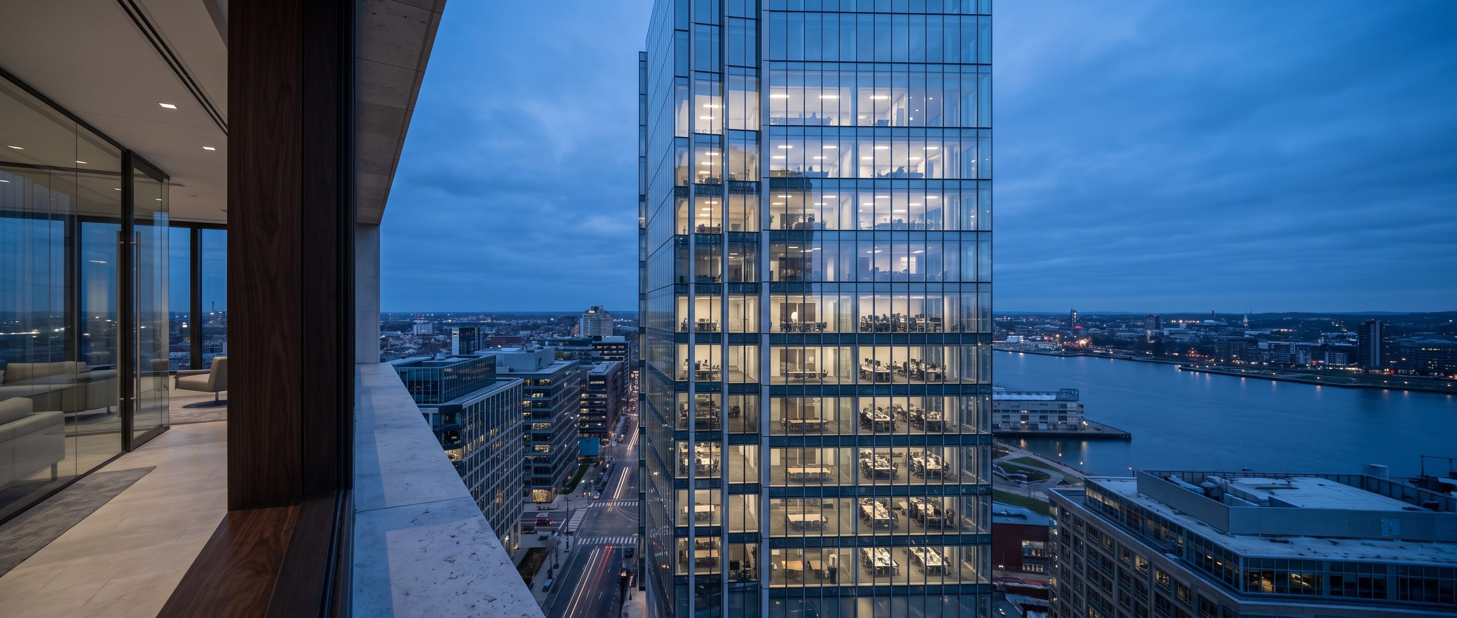A glass office tower at blue hour seen from a high window.