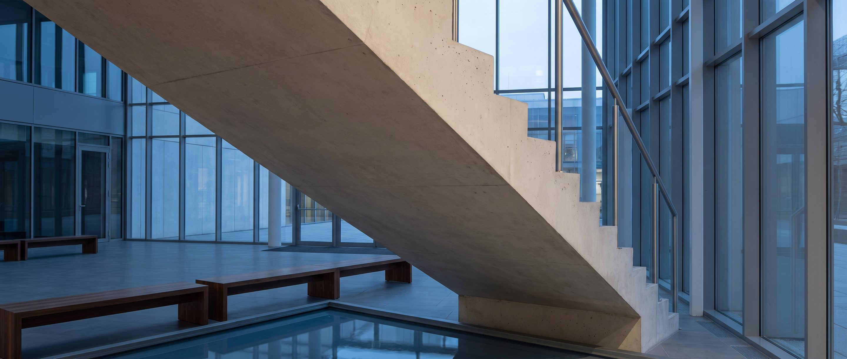 The underside of a pale concrete stair in an empty atrium.