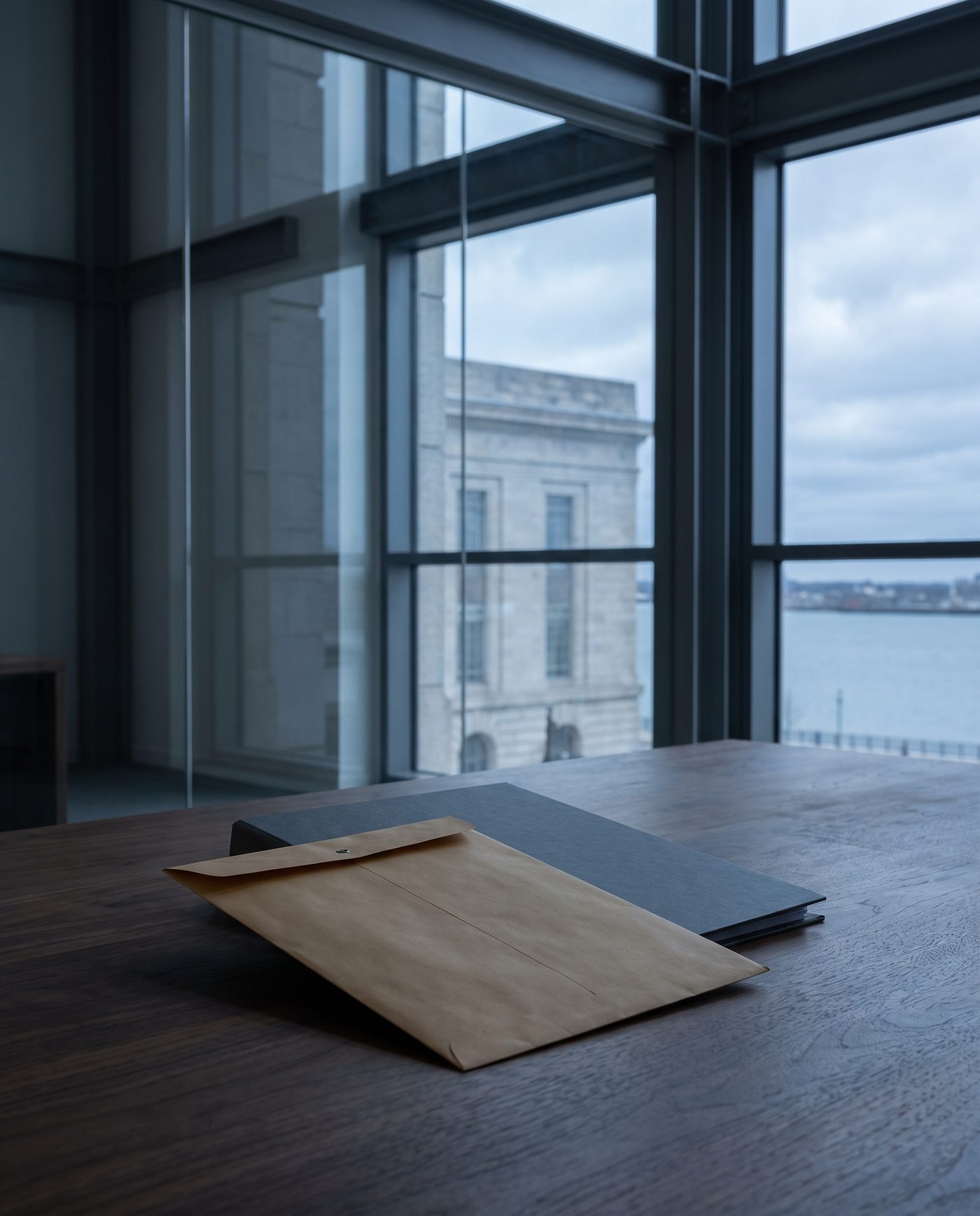 A single sealed envelope propped against a closed folder on a walnut desk.