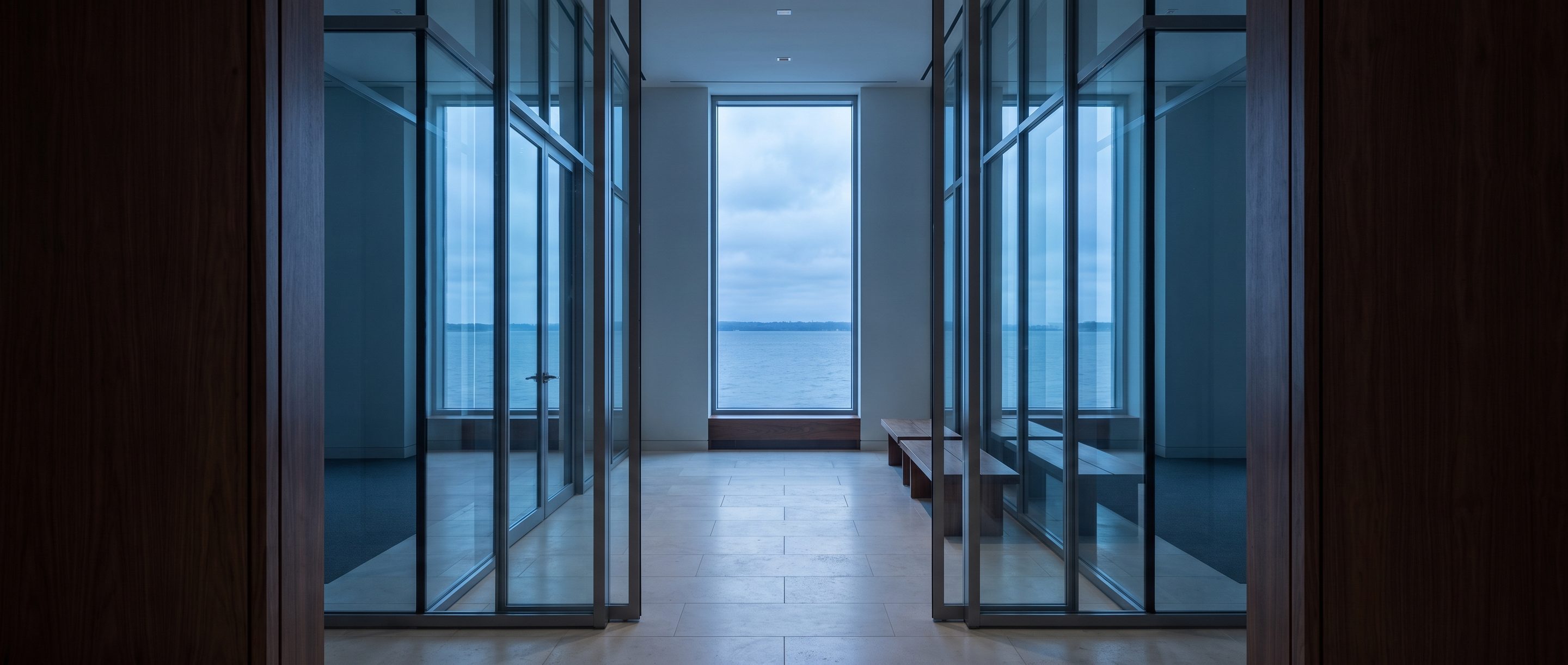 A quiet stone-and-glass office lobby, pale limestone floor.