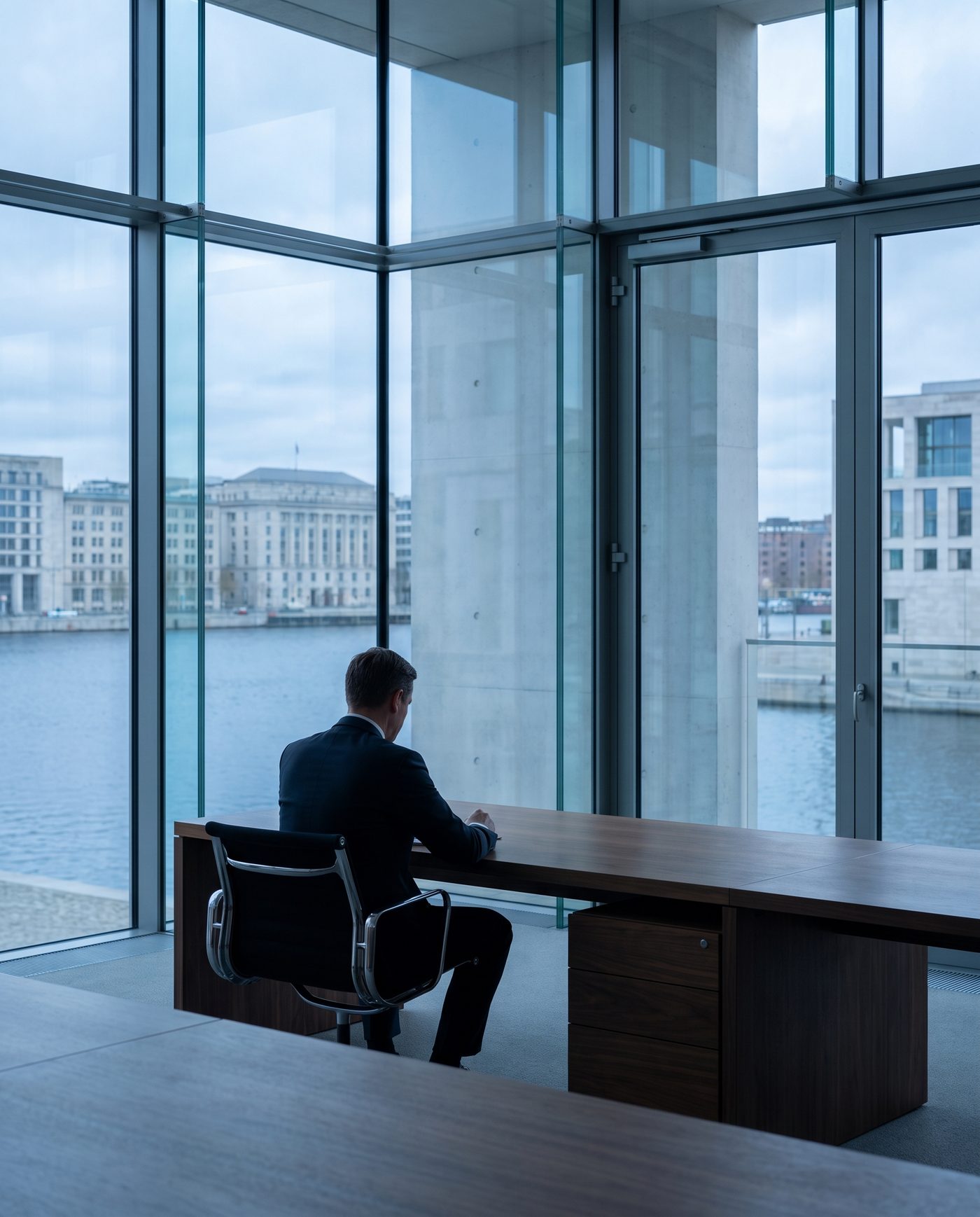 An adult in business dress at a walnut desk, seen from behind.