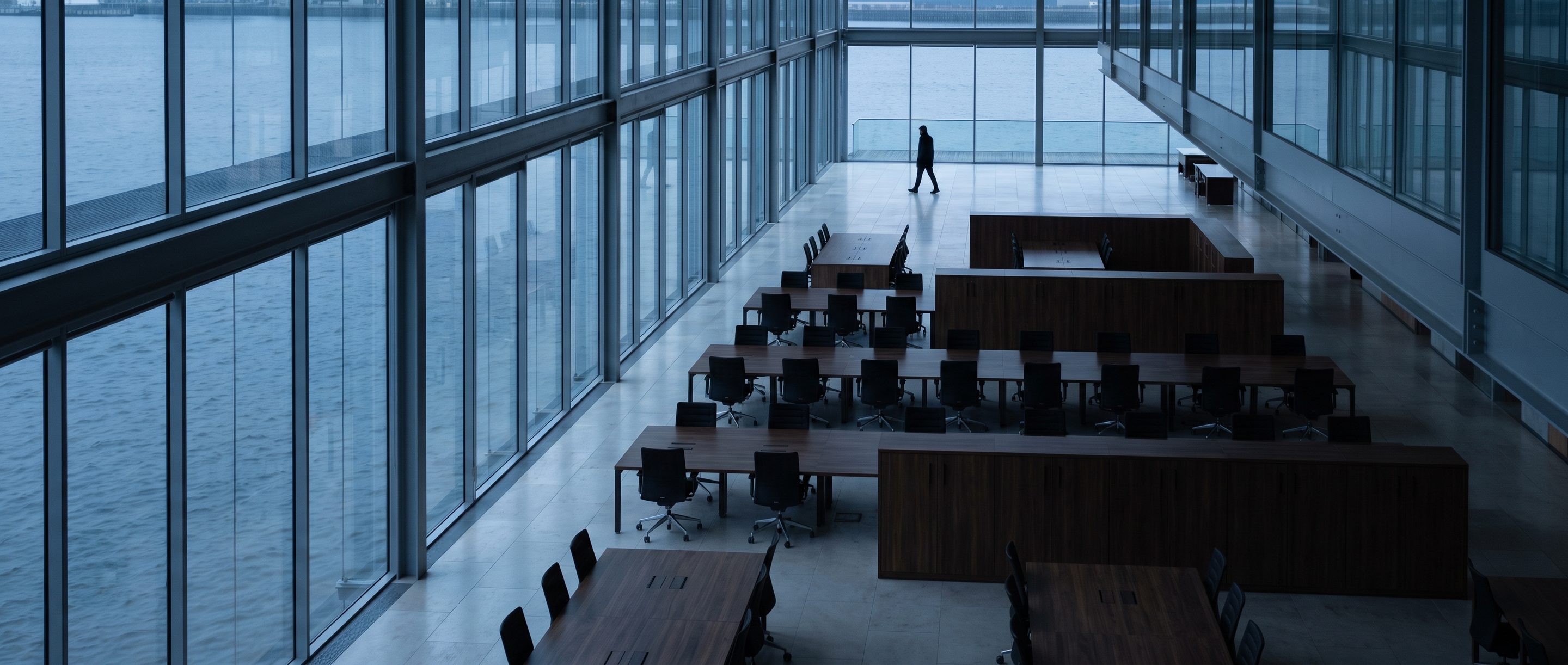 A wide, empty glass-walled office floor, chairs pushed in.