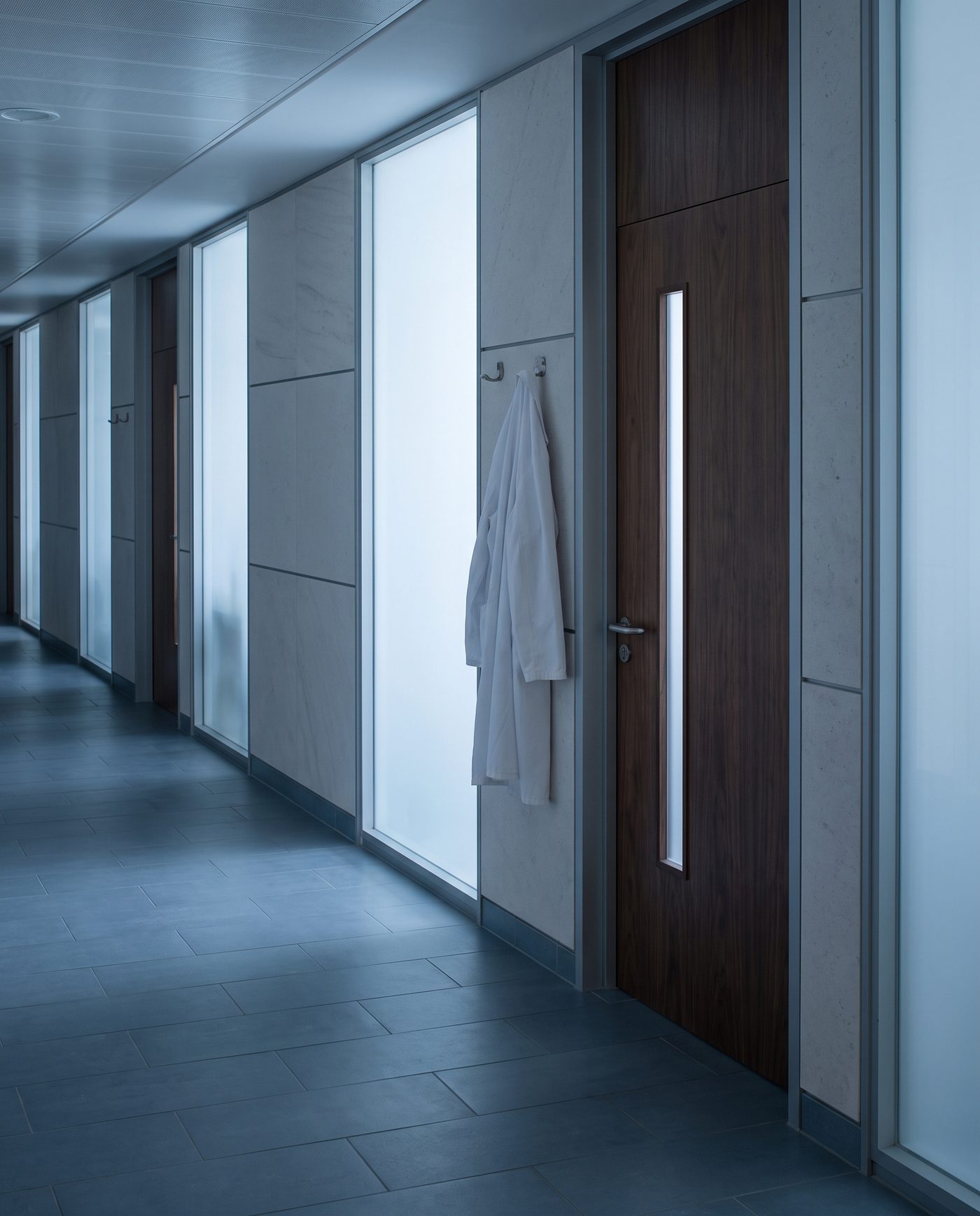 A white coat on a hook beside a closed office door, corridor light.