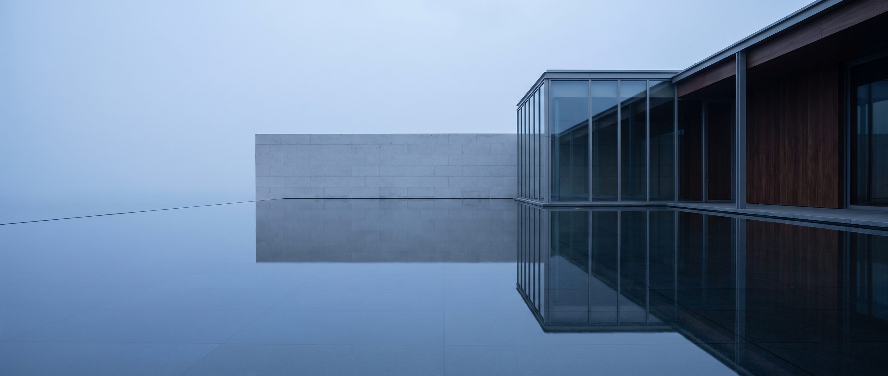 A still reflecting pool against a plain stone wall, overcast light.