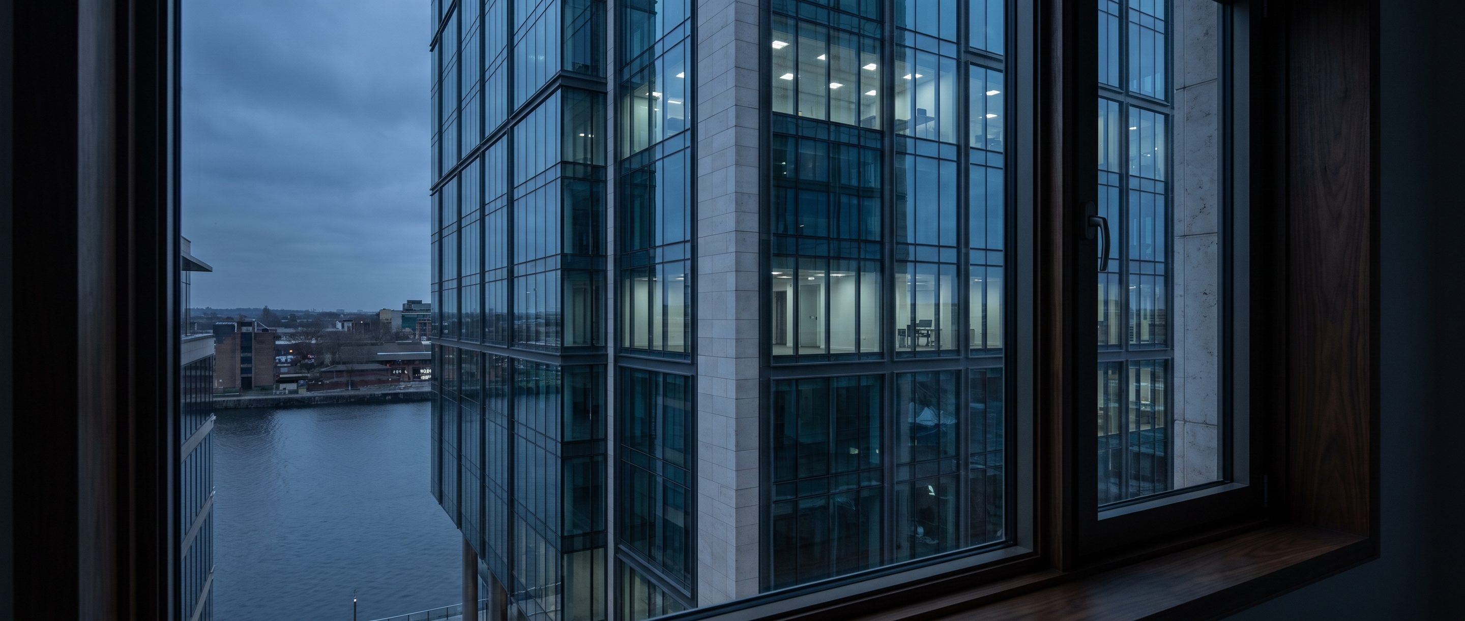 A glass office tower at blue hour seen from a high window.