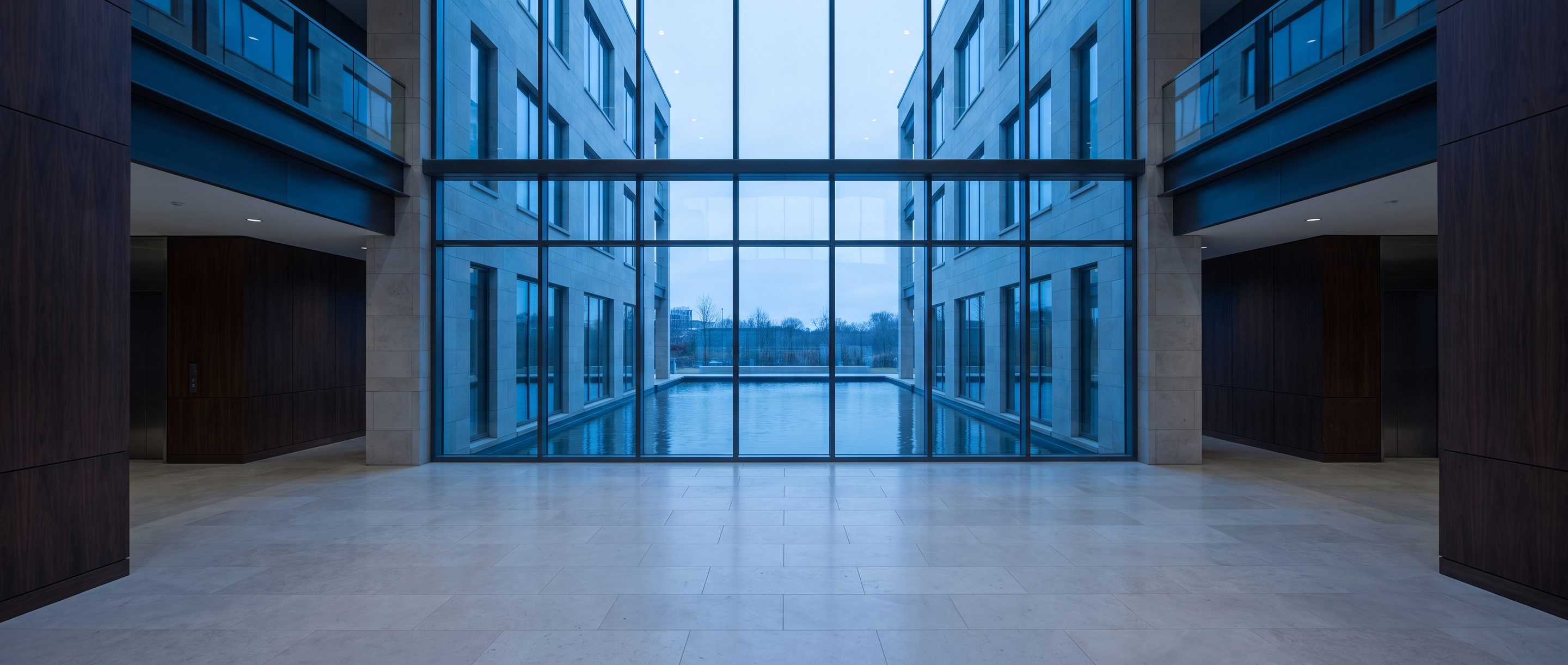A quiet stone-and-glass office lobby, pale limestone floor.