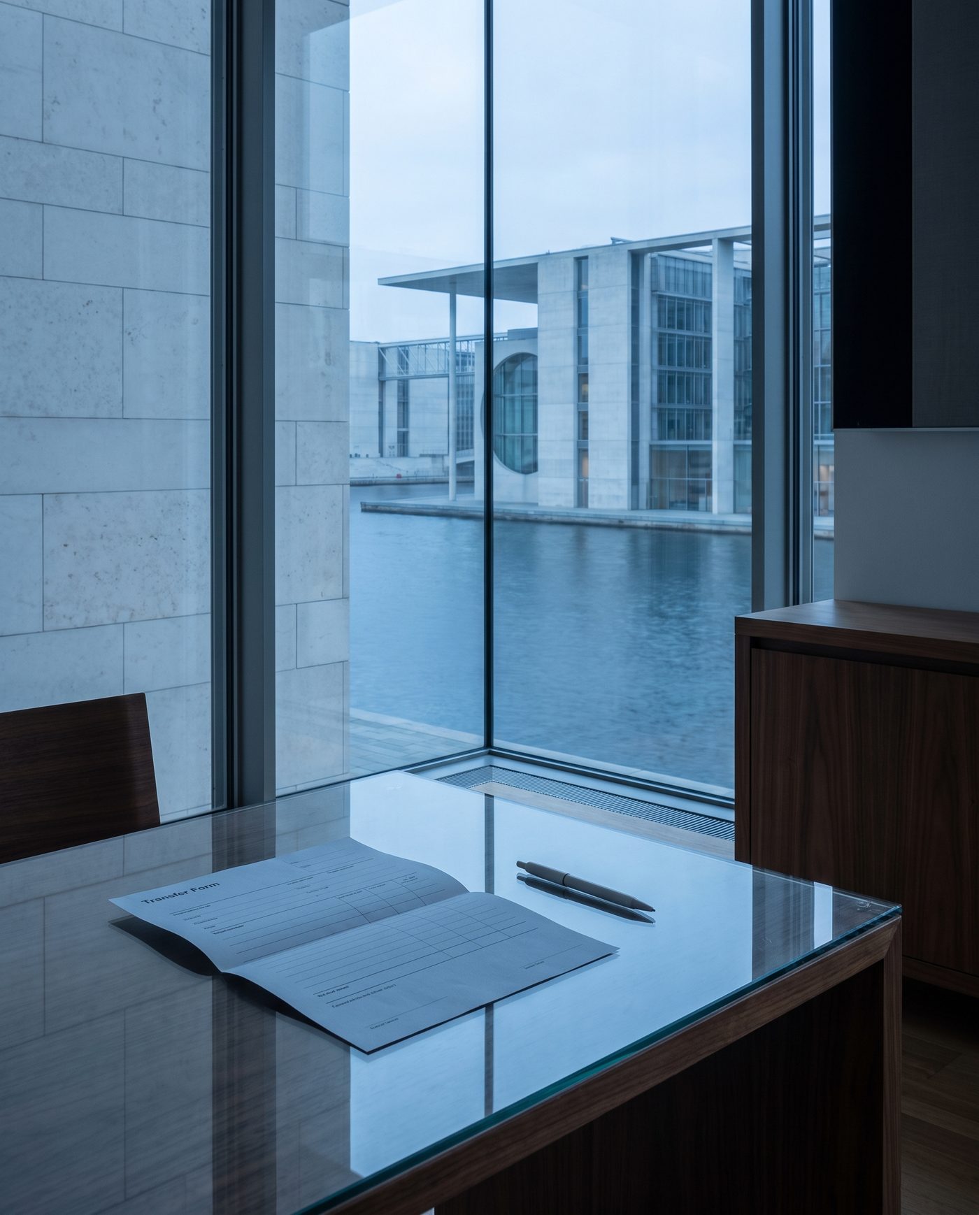 A folded transfer form and a pen resting on a glass-topped table.