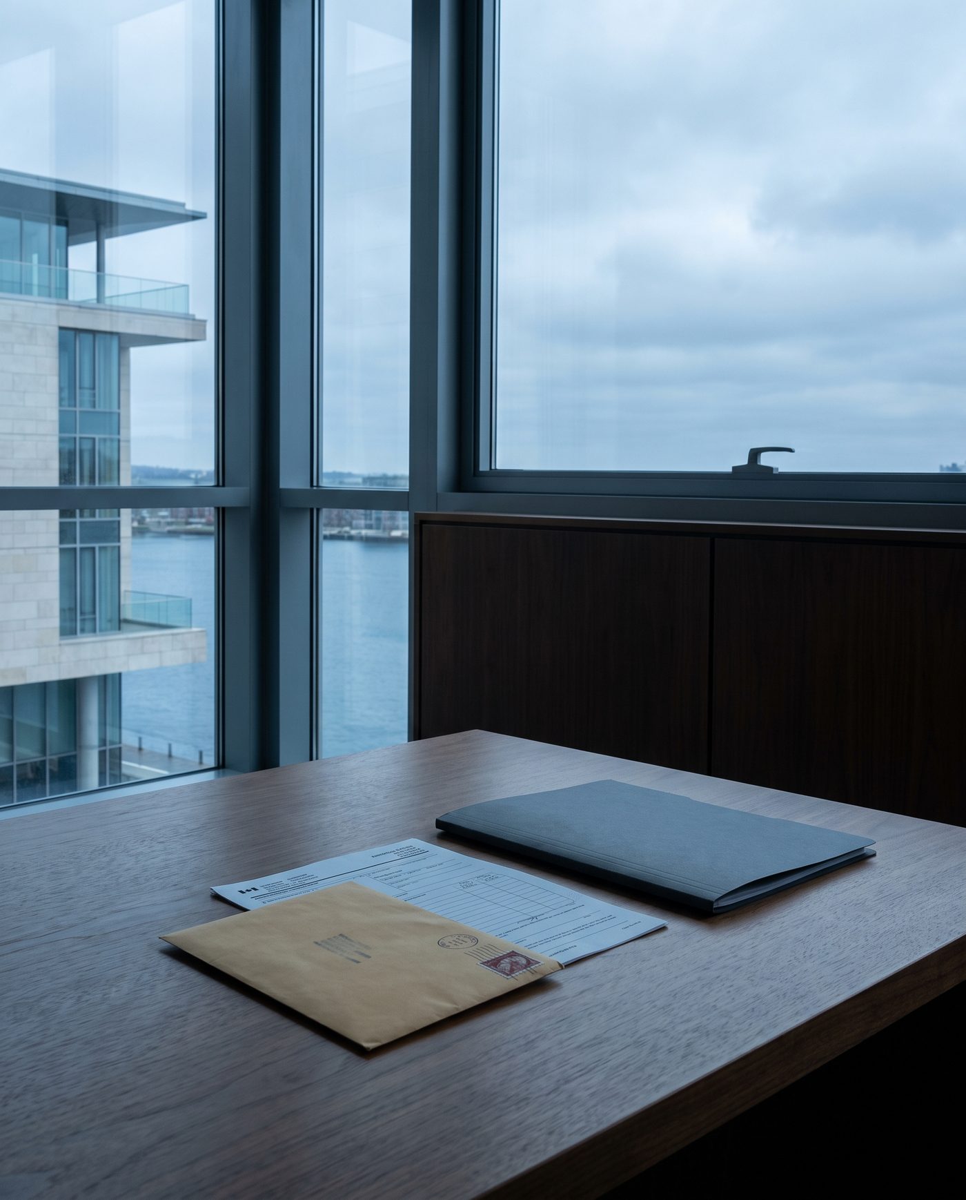 A stamped envelope and a government form on a plain walnut desk beside a closed folder.