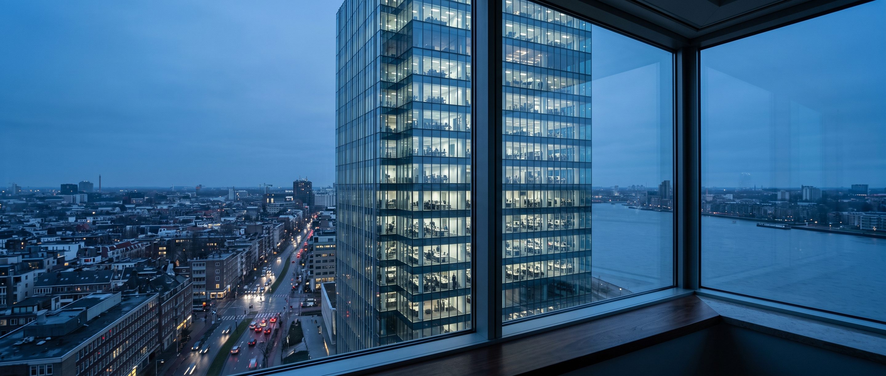 A glass office tower at blue hour seen from a high window.