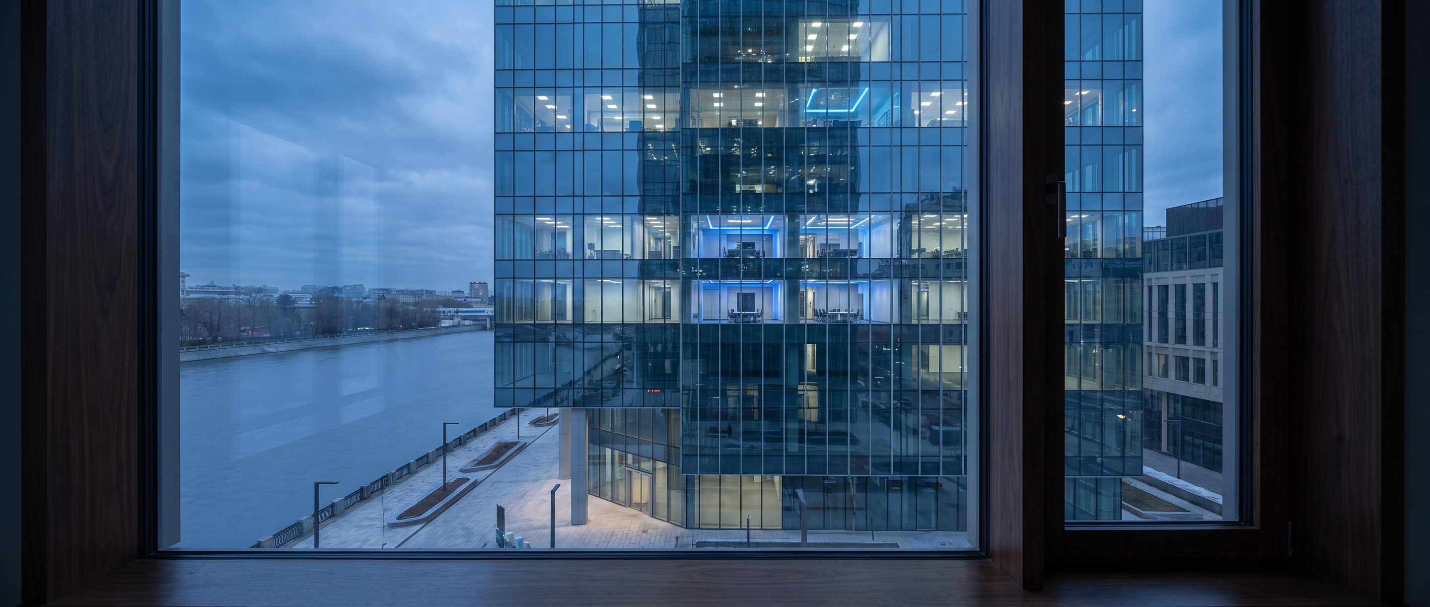 A glass office tower at blue hour seen from a high window.