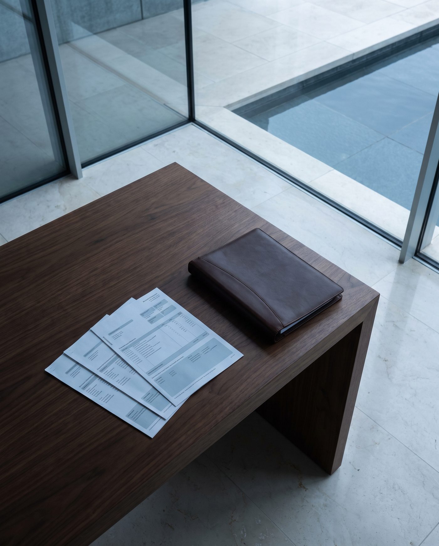 A spread of account statements and a closed leather portfolio binder on a walnut table.