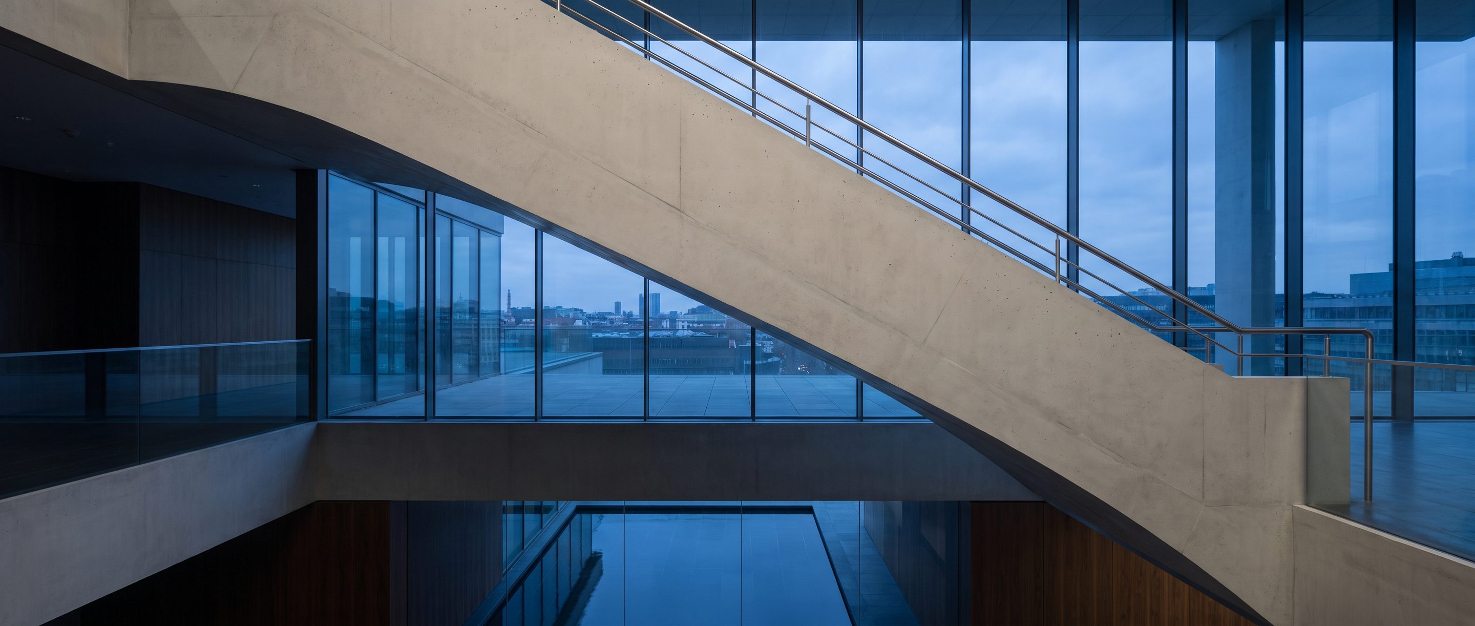 The underside of a pale concrete stair in an empty atrium.